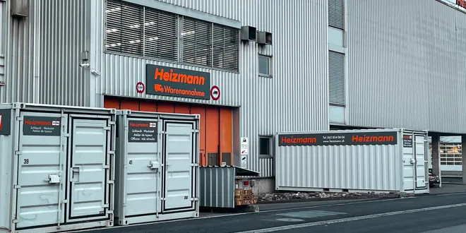  Bâtiment industriel avec logo Heizmann et différents conteneurs devant l'entrée