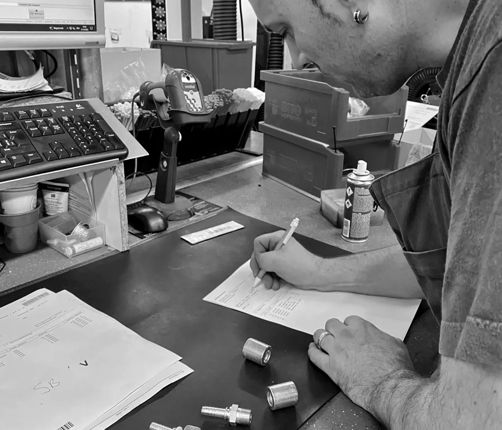 Mitarbeiter prüft Bauteile mit Messwerkzeugen an einem Arbeitstisch in der Werkstatt