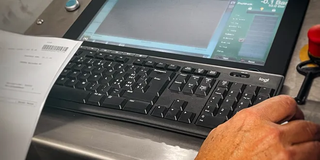 Personne manipulant un terminal informatique de banc d'essai avec clavier et écran sur un plan de travail