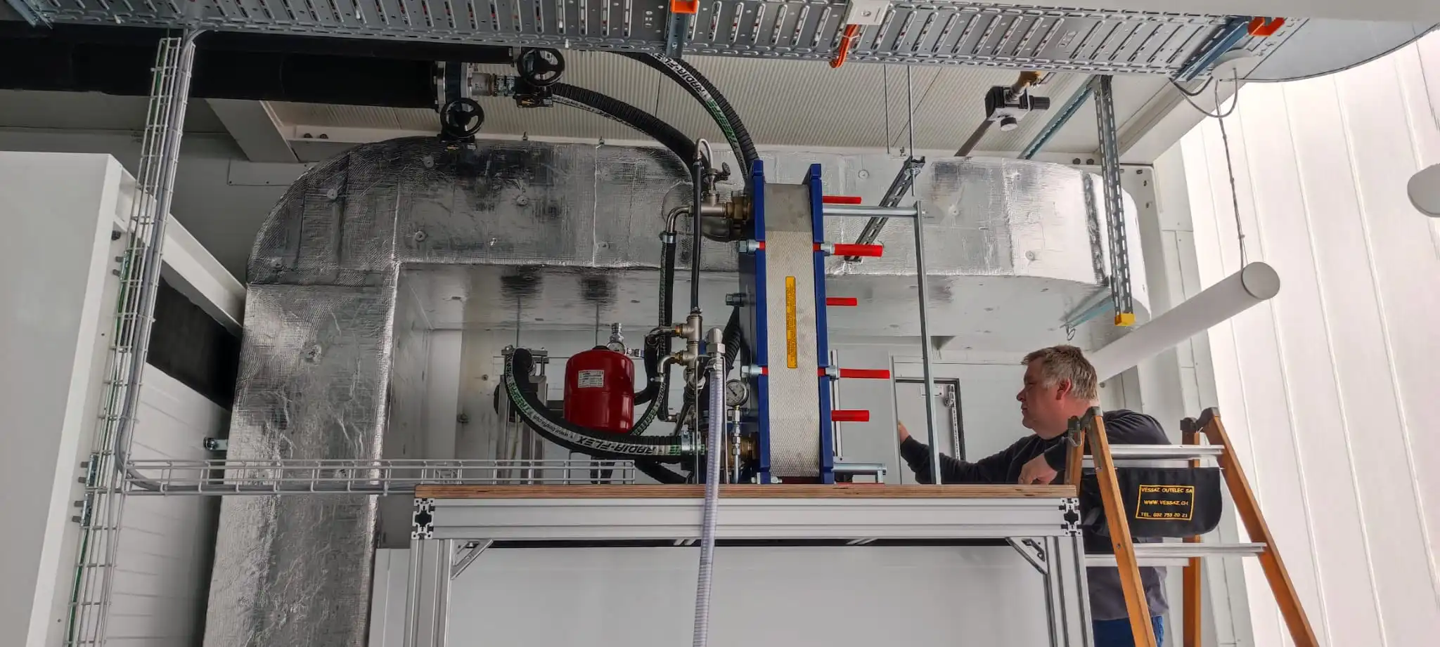 Technicien effectuant la maintenance d'un système de ventilation complexe dans un milieu industriel.