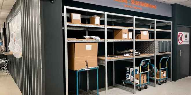 Zone de retrait avec étagères remplies de cartons et deux chariots manuels dans un entrepôt