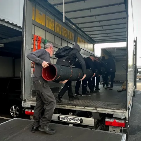 Mehrere Personen laden einen grossen Saugbaggerschlauch von einem LKW