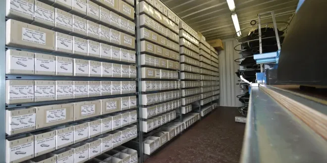 Vue intérieure d'un conteneur avec des étagères pleines de boîtes de stockage étiquetées, dévidoir de tuyau au premier plan, stockage industriel