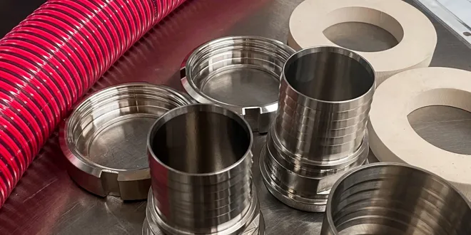 Pièces d'atelier métalliques sur une table, comprenant des tuyaux flexibles rouges, des anneaux métalliques cylindriques et des joints plats avec un document en arrière-plan