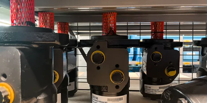 Schwarze Hydraulikpumpen mit roten Schutzkappen aufgereiht auf einem Metallregal.