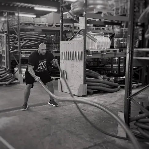 Person beim Training mit einem industriellen Schlauch in einer Industriehalle, Schwarz-Weiss-Aufnahme