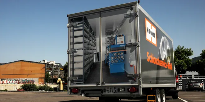 Lkw-Anhänger mit aufgebauter mobiler Werkstatt und Firmenlogo, parkend auf einem Platz, blauer Himmel