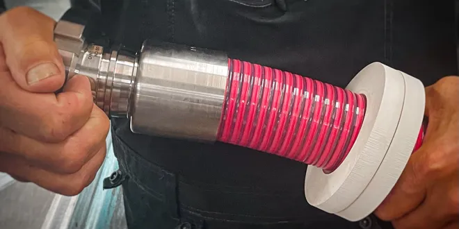 Person montiert einen roten flexiblen Schlauch auf ein metallisches Maschinenteil mit einer weissem Aufprallschutz