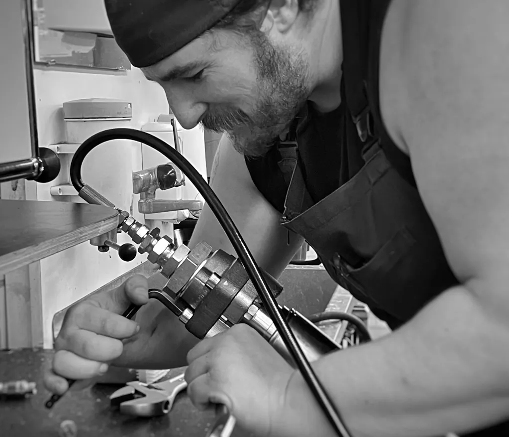 Mann mit Bandana und Tanktop arbeitet konzentriert an einer Metallvorrichtung in einer Werkstatt