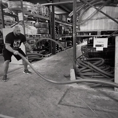 Person beim Training mit einem industriellen Schlauch in einer Industriehalle, Schwarz-Weiss-Aufnahme