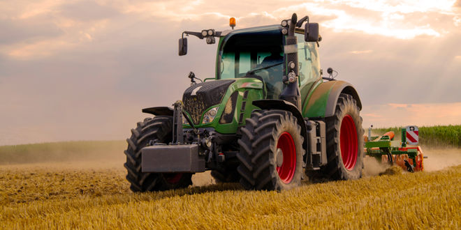 Grüner Traktor auf einem Weizenfeld bei Sonnenuntergang, der Landwirtschaftsgeräte zieht.