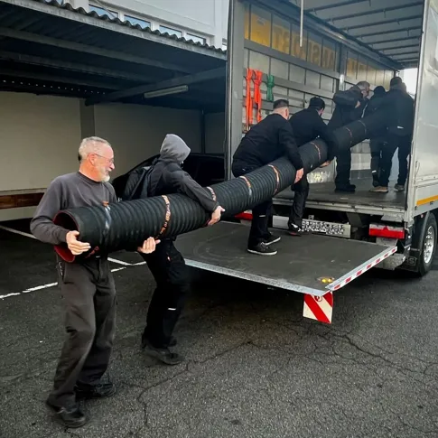 Mehrere Personen laden einen grossen Saugbaggerschlauch von einem LKW